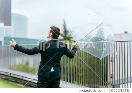 Foreign businessman holding an umbrella on a rainy day (rainy season, typhoon, after rain, abnormal weather) Foreign businessman holding an umbrella on a rainy day (rainy season, typhoon, after rain, abnormal weather) 109225976