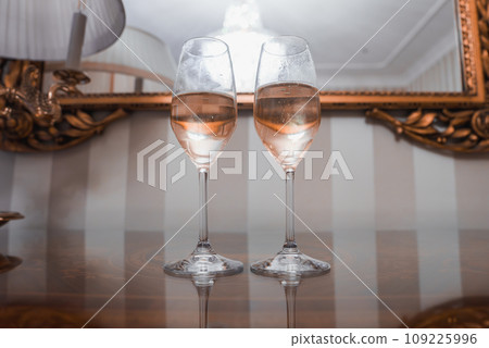 Two elegant champagne flutes placed on a table in front of a mirror, creating a sense of luxury and sophistication. Unknown location and specific details. 109225996