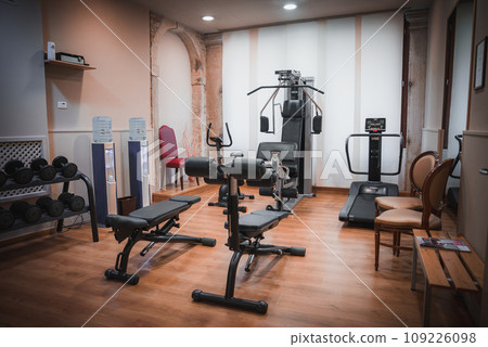 Modern gym room with exercise equipment including a rowing machine, captured from a side angle. No flooring or windows are visible. Modern gym room with exercise equipment including a rowing machine, captured from a side angle. No flooring or windows are visible. 109226098