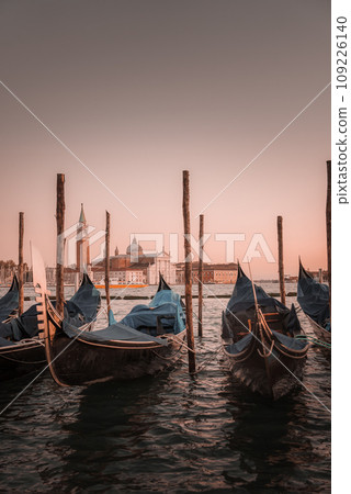 Tranquil sunset scene of gondolas reflected in calm waters. No people or birds present. Part of a collection showcasing popular places in Venice, Italy. 109226140