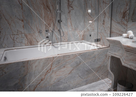 Luxurious bathroom with marble walls, white bathtub, sink, and shower in Venice, Italy. Opulent space with no artwork or window, likely part of a high-end hotel or restaurant. 109226427