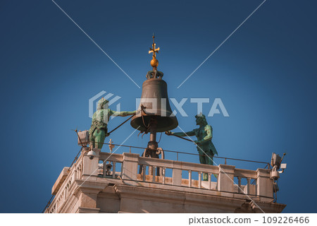 Two statues with a bell on top of a building in Venice, Italy. The material and significance of the statues are unknown. No visible wear or damage. Two statues with a bell on top of a building in Venice, Italy. The material and significance of the statues are unknown. No visible wear or damage. 109226466