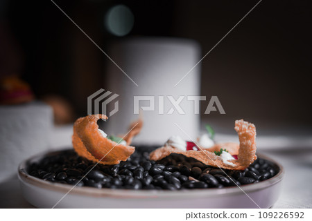 A close-up shot of a plate of black beans on a table. The type of cuisine and other food on the plate are unknown. 109226592