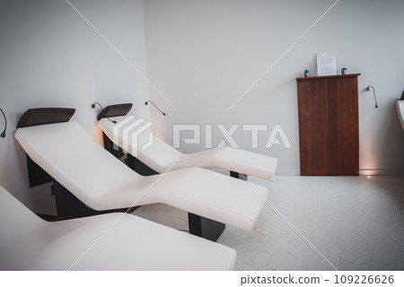 A serene and tranquil room with a row of white lounge chairs, creating a relaxing and quiet atmosphere. The minimalist aesthetic offers a space for relaxation and comfort. A serene and tranquil room with a row of white lounge chairs, creating a relaxing and quiet atmosphere. The minimalist aesthetic offers a space for relaxation and comfort. 109226626