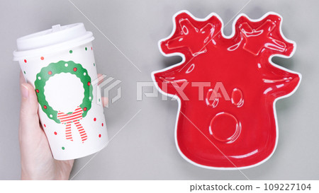Festive table setting with red plate in Christmas raindeer shape and dispozable paper coffee cup on grey background. Holiday table decoration Top view. Space for text. 109227104