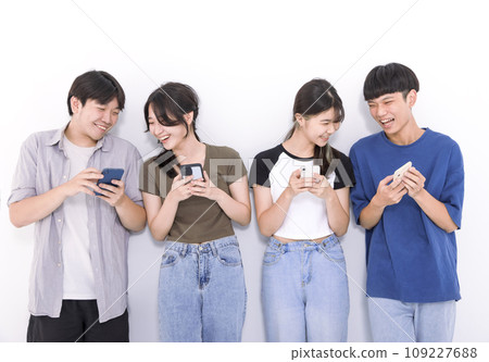Group of stylish students using mobile phone stand before white background Group of stylish students using mobile phone stand before white background 109227688