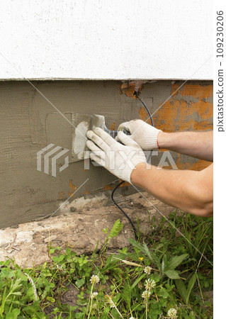 A worker plasters the foundation with cement plaster and glues in the mesh. Finishing the house with cement plaster A worker plasters the foundation with cement plaster and glues in the mesh. Finishing the house with cement plaster 109230206