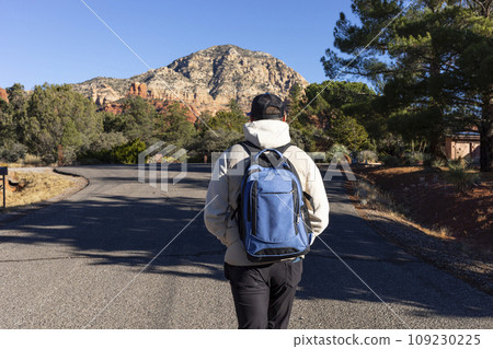 Back View of Male Tourist with Backpack Walking the Road Towards Red Rock Mountain Butte Of Sedona, Arizona, USA Beautiful Scenic Landscape. Tourism and Attraction, Spiritual Place. Horizontal Back View of Male Tourist with Backpack Walking the Road Towards Red Rock Mountain Butte Of Sedona, Arizona, USA Beautiful Scenic Landscape. Tourism and Attraction, Spiritual Place. Horizontal 109230225