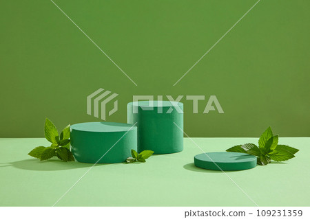Against a green background, three cylinder podiums displayed with spearmint leaves. Blank space for the presentation of cosmetic products. Spearmint leaves are a commonly used ingredient in herbal tea 109231359