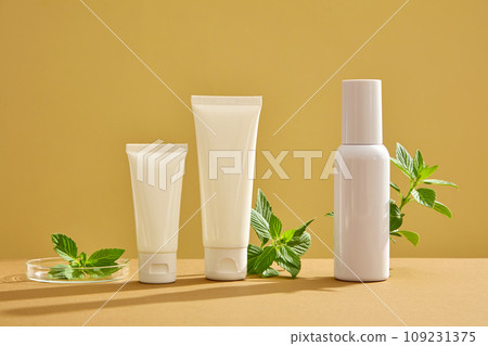Front view of cosmetic bottles with different shape displayed on brown background with leaves of spearmint. Mockup scene for advertising. Space for design 109231375