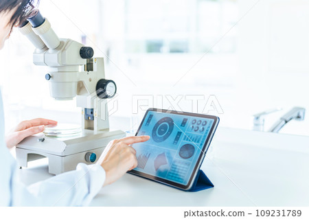 A woman in a white coat researching using a microscope and a tablet A woman in a white coat researching using a microscope and a tablet 109231789