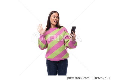young pretty caucasian woman with black hair dressed in a pink sweater uses a mobile phone on a young pretty caucasian woman with black hair dressed in a pink sweater uses a mobile phone on a 109232527