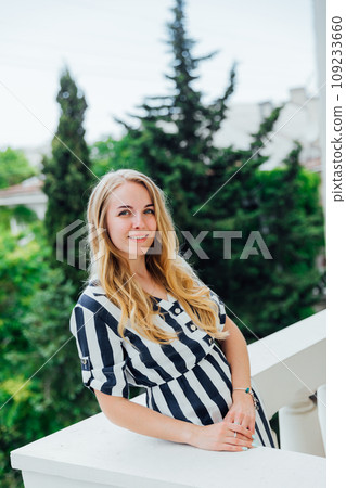 woman in striped dress standing on balcony looking at street woman in striped dress standing on balcony looking at street 109233660