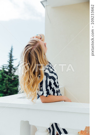 woman in striped dress standing on balcony looking at street woman in striped dress standing on balcony looking at street 109233662