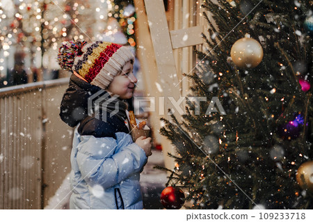 Cute little boy eating churros on traditional Christmas fair in snow. Child kid enjoying sweets on Xmas market. Winter holidays with family. Merry Christmas 109233718