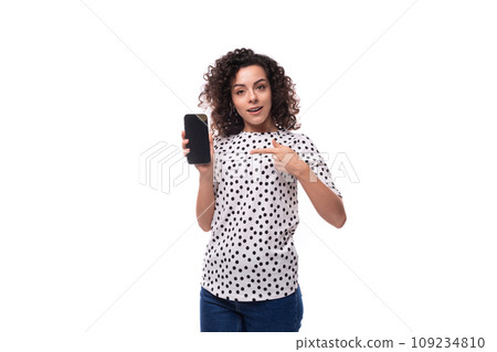 young stylish woman with curly hair dressed in a blouse with polka dots shows a smartphone with a 109234810