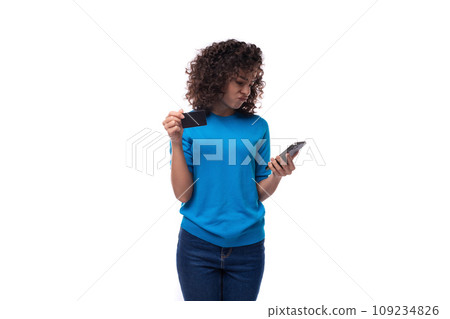 a young woman with a curly hairstyle above her shoulders holds a smartphone and a plastic card with a young woman with a curly hairstyle above her shoulders holds a smartphone and a plastic card with 109234826