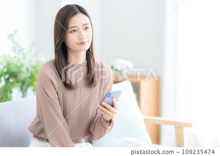 年輕女子在客廳的沙發上使用智慧型手機 109235474