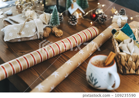 Preparing Christmas eco gift. Wrapping paper, wicker basket, coffee cup. Unprepared presents on wooden table with natural decor elements and items Christmas packing wrapping Concept 109235590
