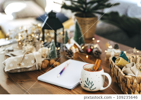 Woman hand holding pen on notepad at home on winter holidays xmas. Goals plans make to do and wish list for new year christmas concept, girl writing in notebook. Christmas decoration, gift boxes 109235646