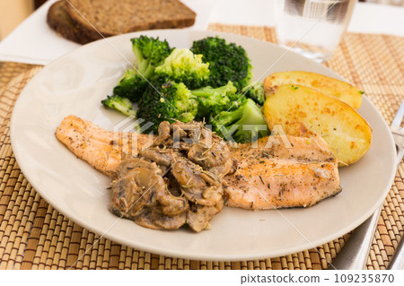 Fried river trout fillet with a complex side dish of broccoli, baked potatoes and mushroom sauce 109235870