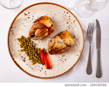 Roasted whole quails served on plate with peas and fried carrot 109236588