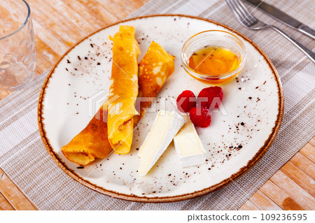 Portion of rolled pancakes with raspberries, honey and pieces of cheese 109236595