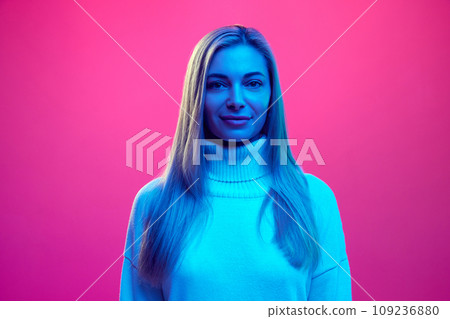 Close up portrait of young attractive smiling woman in knitted warm sweater against pink background in blue neon light. Close up portrait of young attractive smiling woman in knitted warm sweater against pink background in blue neon light. 109236880