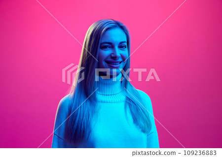 Close up portrait of young attractive smiling, laughing woman in knitted warm sweater against pink background in neon light. concept of human emotions. 109236883