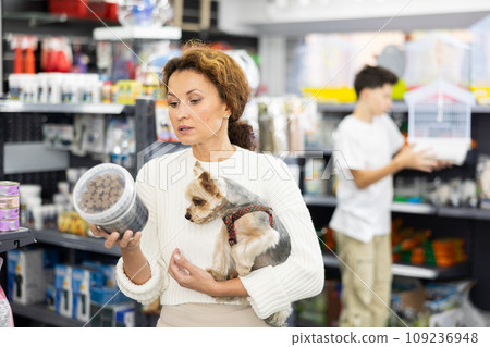 Buyers woman with Yorkshire Terrier choose healthy food and nutrition for pet in tin can 109236948