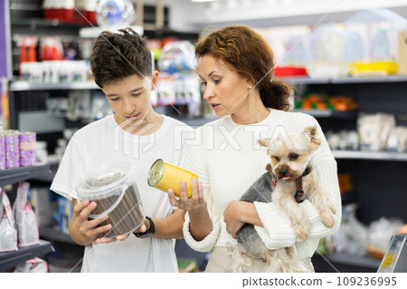 Teenager with mother and Yorkshire terrier choosing dog food in store 109236995