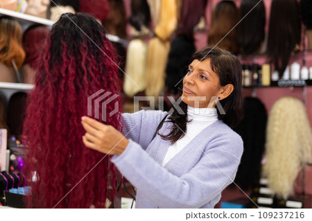 Latin american woman choosing natural hair wig at specialty boutique Latin american woman choosing natural hair wig at specialty boutique 109237216