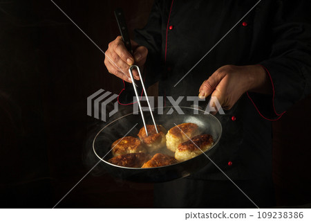 Frying delicious pancakes for breakfast. A hot frying pan in the cook's hand and a fork. Black space for menu or recipe 109238386