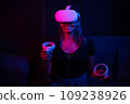 Young asian woman using at home Virtual Reality headset with joysticks playing VR video games, neon pink blue light 109238926