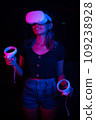 Young asian woman using at home Virtual Reality headset with joysticks playing VR video games, neon pink blue light 109238928