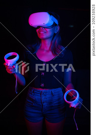 Young asian woman using at home Virtual Reality headset with joysticks playing VR video games, neon pink blue light 109238928