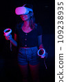 Young asian woman using at home Virtual Reality headset with joysticks playing VR video games, neon pink blue light 109238935