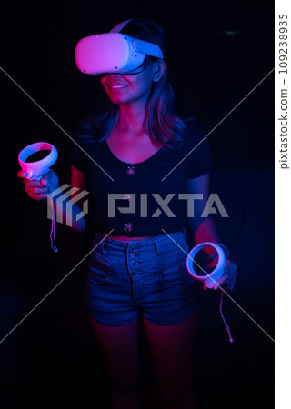 Young asian woman using at home Virtual Reality headset with joysticks playing VR video games, neon pink blue light 109238935