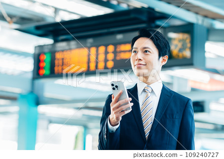 一位商人在車站看著智慧型手機。照片由京王電鐵株式會社提供。 一位商人在車站看著智慧型手機。照片由京王電鐵株式會社提供。 109240727