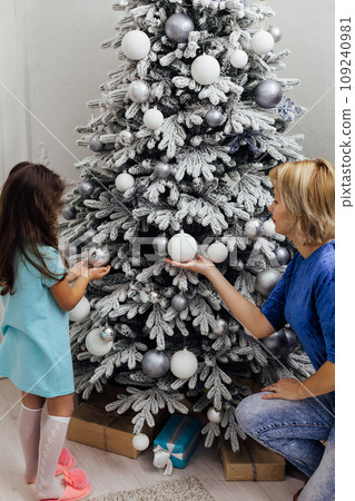Mom and daughter at the christmas tree with gifts and toys for the new year 109240981