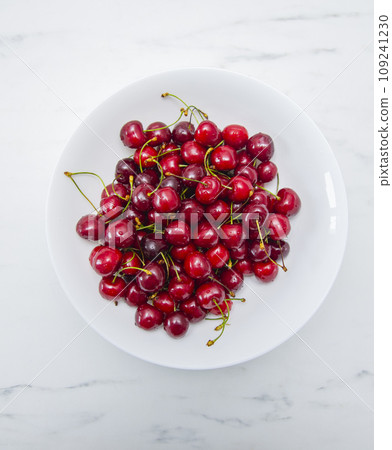 Fresh red cherries fruit on a white plate on a white surface 109241230