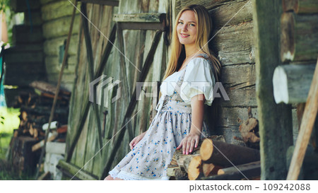A girl of Slavic appearance poses in the countryside by the barn. A girl of Slavic appearance poses in the countryside by the barn. 109242088