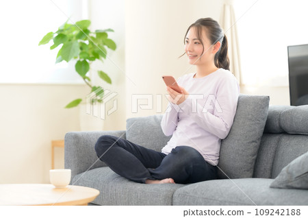 一個女人坐在沙發上，看著她的智能手機 109242188