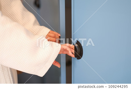 Women hands in bathrobe opening doors of blue wardrobe at home closeup 109244295