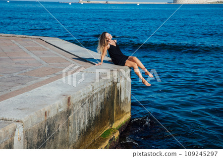Beautiful woman in black summer dress on a walk by the sea Beautiful woman in black summer dress on a walk by the sea 109245297