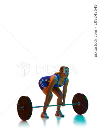 Young woman, athlete in motion, training, lifting heavy weights, barbell against white background in neon light 109245649