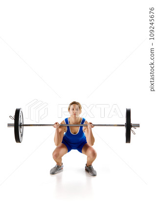 Concentrated strong young woman, athlete training doing squats, lifting heavy barbell against white background 109245676