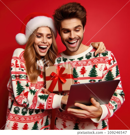 funny sweet young loving couple dressed print pullover buying christmas gifts typing modern gadget on red color background funny sweet young loving couple dressed print pullover buying christmas gifts typing modern gadget on red color background 109246547
