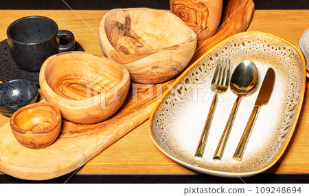 Beautiful still life of handmade wooden and earthenware dishes with gilded metal cutlery. 109248694