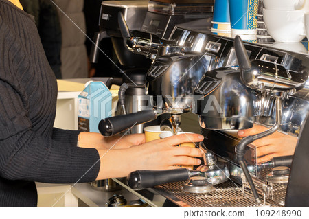 The woman barista prepares coffee in a coffee machine and pours it into paper cups. The woman barista prepares coffee in a coffee machine and pours it into paper cups. 109248990